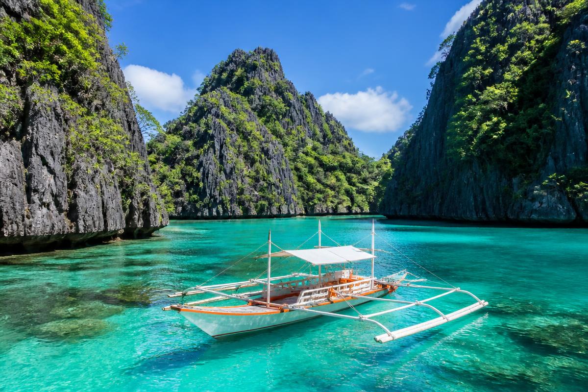 Outrigger boat on a turquoise lagoon between limestone cliffs in Palawan