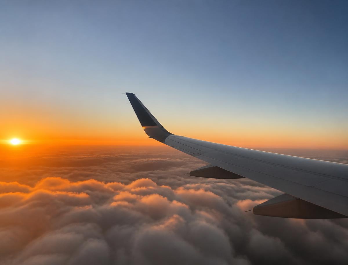 Aircraft wing above golden clouds at sunset